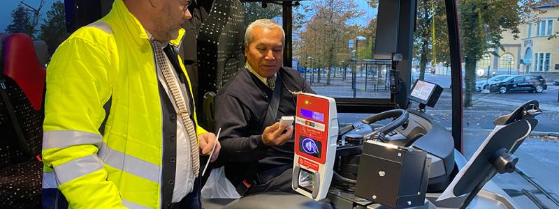 Förarcoach Åke Håkansson ger bussföraren René Alvarez en tablettask i kampanjen ”Bälte på, mobilen av”. Foto: Bergkvarabuss