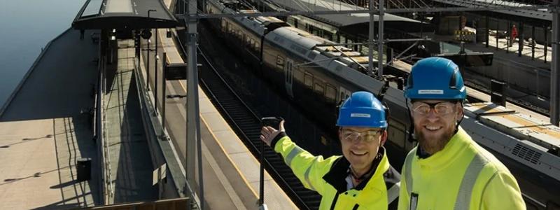 Infrastrukturarbeten vid Drammens station i Norge. Geir Boman Rinde (till vänster) och Morten E. Paulsen är båda byggledare för el på stationen. De visar glatt upp de första solpanelerna som installerades på plattformstaket vid floden.
Foto: Anne Mette Storvik, Bane NOR