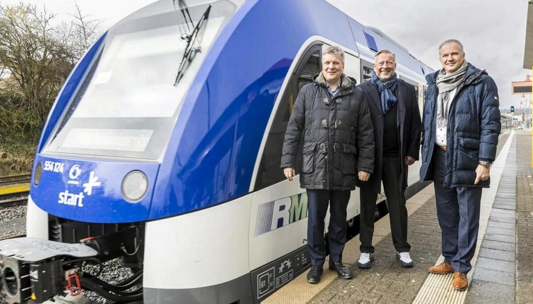Tyska kollektivtrafikbolaget satsar på tillfälliga lösningar för RB15-linjen. Rhein-Main-Verkehrsverbund (RMV) står inför en utmanande period när bränslecellsdrivna tåg på RB15-linjen ersätts med dieseldrivna enheter under hela 2025. På bilden ses RMV:s styrelseordförande Ulrich Krebs, verkställande direktör Knut Ringat och Usingens borgmästare Steffen Wernard vid Usingen station tillsammans med ett tåg från RB15-linjen. 
De bränslecellsdrivna tågen, som infördes för att minska beroendet av fossila bränslen, har visat sig vara opålitliga under sina två första år i drift. Det har lett till omfattande trafikstörningar och nödlösningar med dieseldrivna tåg. RMV arbetar nu med tillfälliga lösningar för att säkerställa stabil trafik för passagerarna på linjen. Foto: Arne Landwehr/RMV