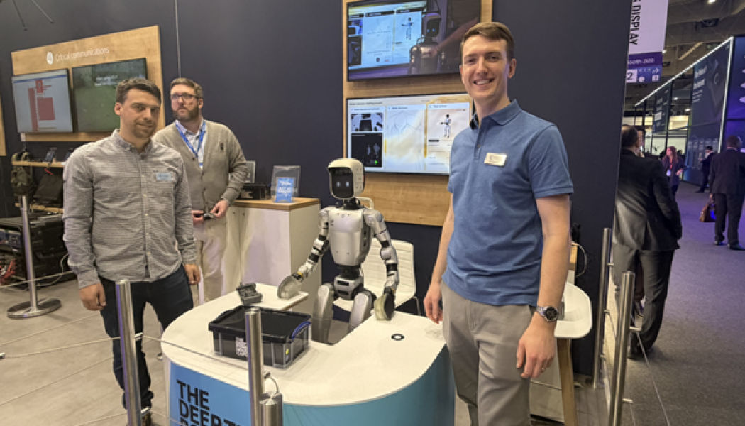 Dom Rugg-Gunn (till höger), robotikingenjör på Cambridge Consultants, vid bolagets monter på MWC 2026. Den humanoida roboten mellan teammedlemmarna är den som under mässan demonstrerade hur AI kan tolka mänskliga gester och plocka upp objekt. Foto: Nicholas Christiansen. 
